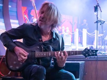 Guitarist with blonde hair under blue and purple stage lighting